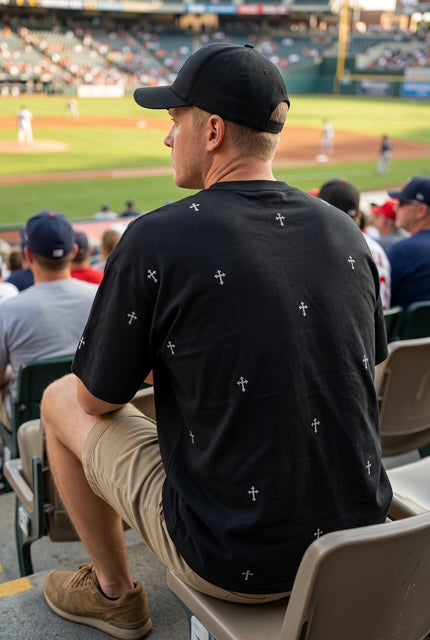 Man from behind wearing a hat at a baseball game wearing The Cross dropped shoulder max weight tee shirt in black hand illustrated cross pattern design-Fox and Form. Fox and Form The Men's Signature Collection.  