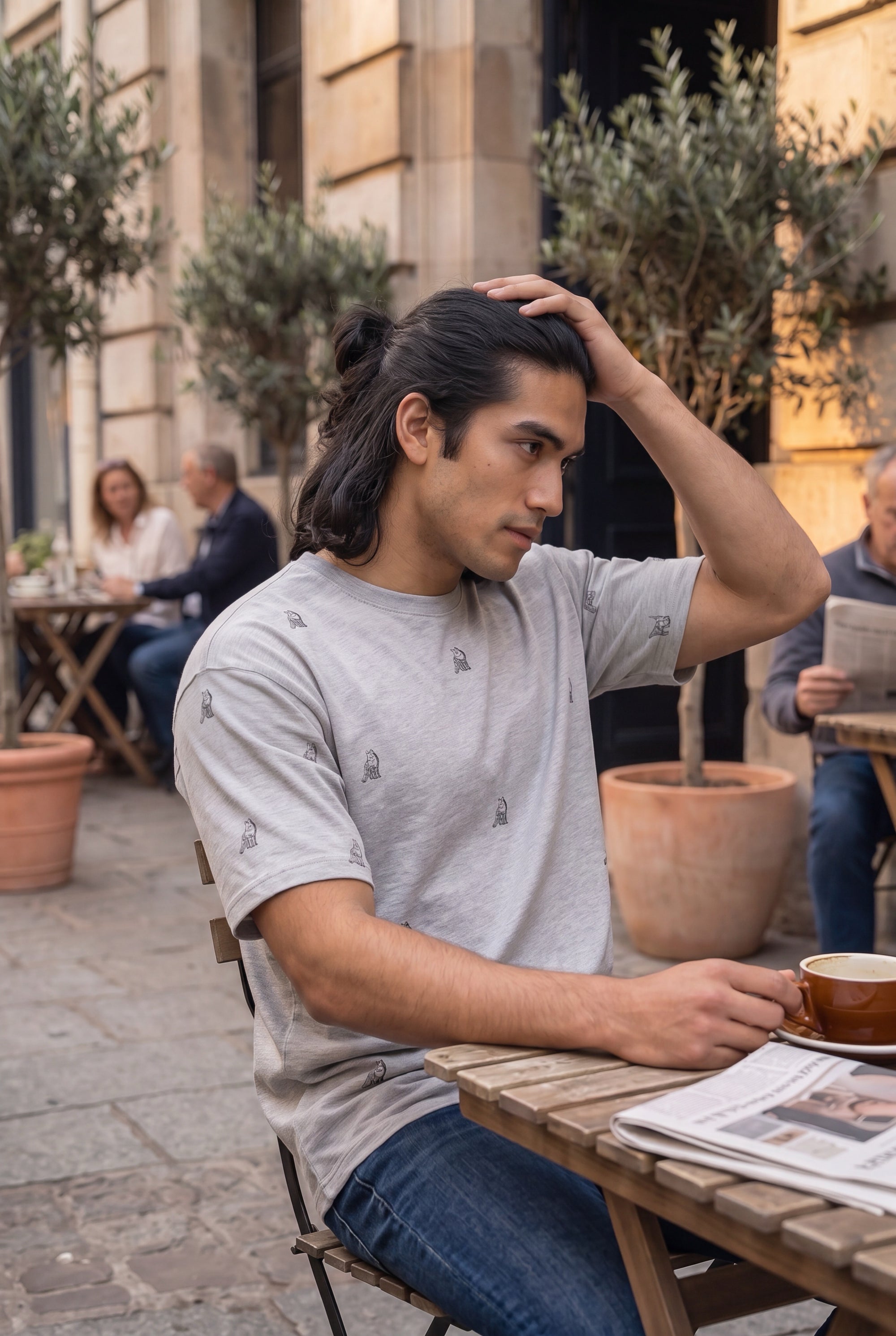 Man wearing Fox and Form The Fox sports grey dropped shoulder max weight tee shirt with hand-etched illustrated fox pattern design, seated at an outdoor café reading a newspaper. Fox and Form Men's Signature Collection. 