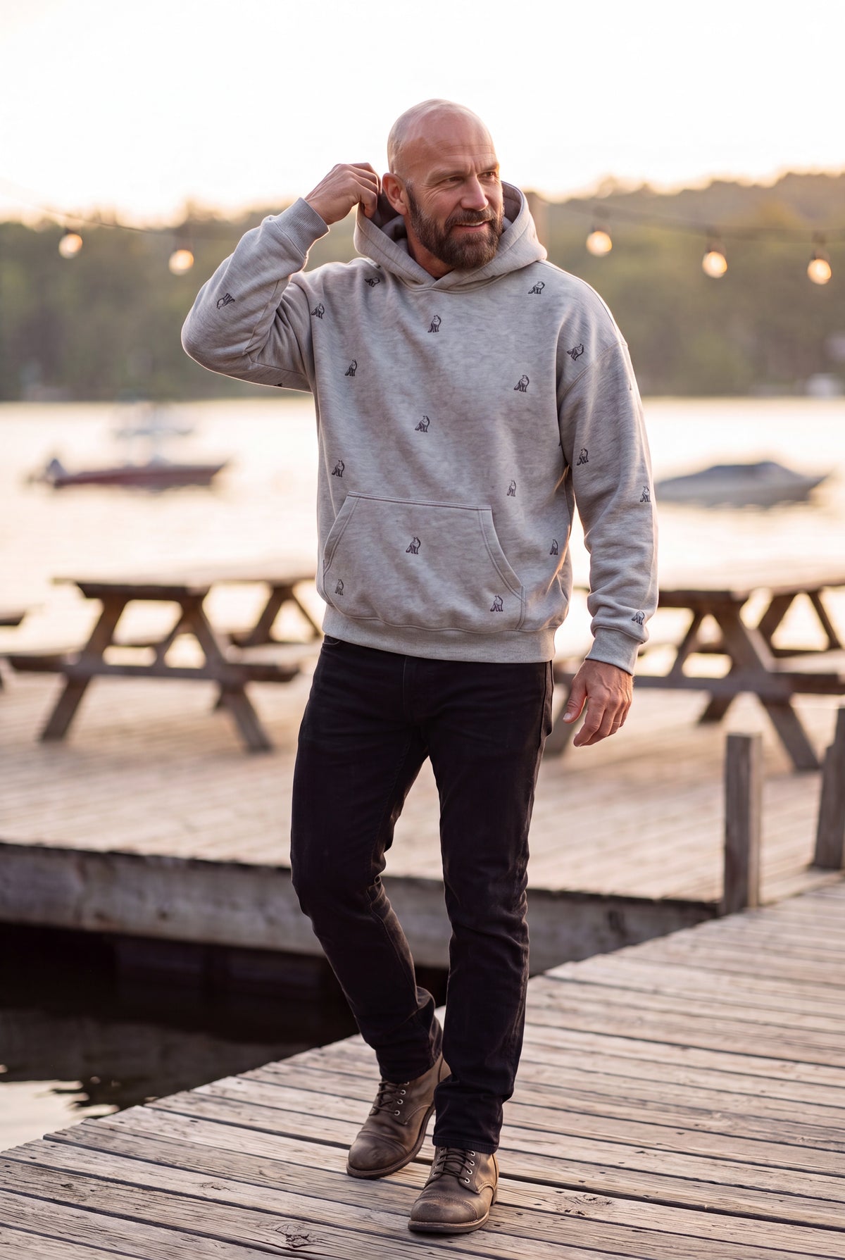 Man wearing Fox and Form The Fox sports grey max weight hooded sweatshirt with hand-etched illustrated fox pattern design, walking on a waterfront deck at golden hour. Fox and Form Men's Signature Collection. 