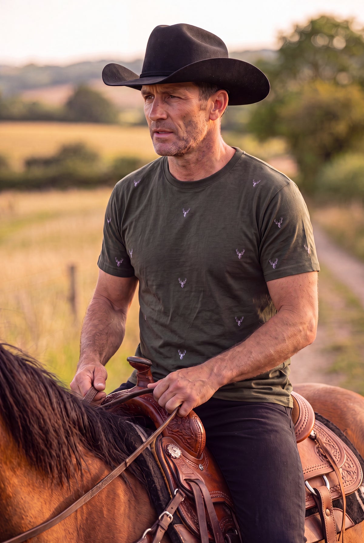 A man wearing Fox and Form The Stag Forest green classic fit ring spun tee shirt with hand-etched illustrated stag pattern design, riding a horse at golden hour in an open field. Fox and Form Men's Signature Collection. 