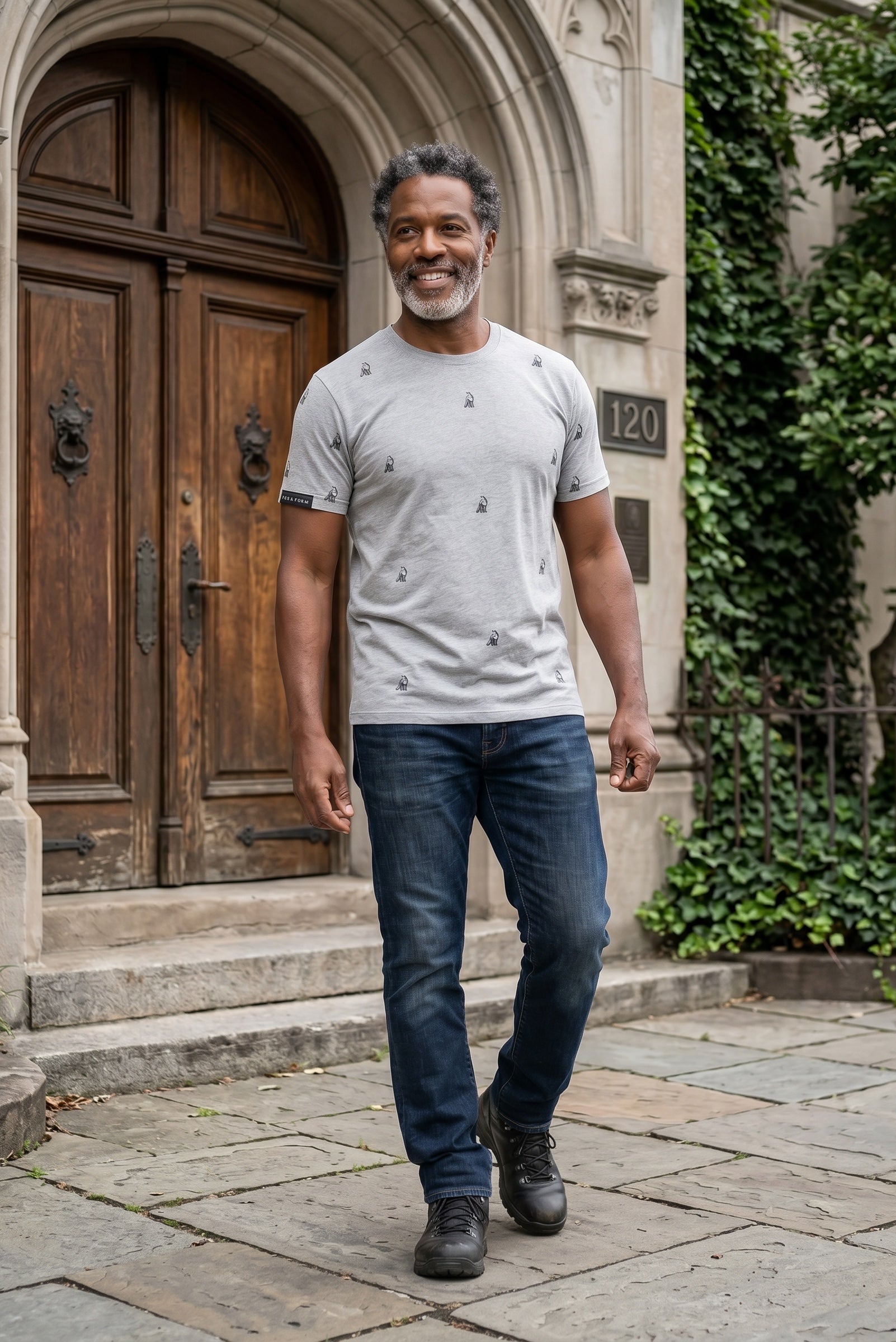 Man wearing Fox and Form The Fox sports grey classic ring spun tee with hand-etched illustrated fox pattern design, walking past a stone archway entrance in an urban neighborhood. Fox and Form Men's Signature Collection. 