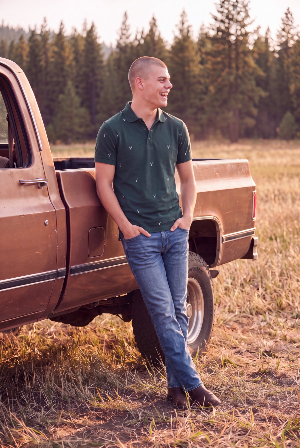 A man wearing a dark green short-sleeve polo shirt with small deer heads patterned across the front and back and blue jeans stands leaning against the side of a brown pickup truck in an outdoor grassy field with a forest in the background. Fox & Form 
