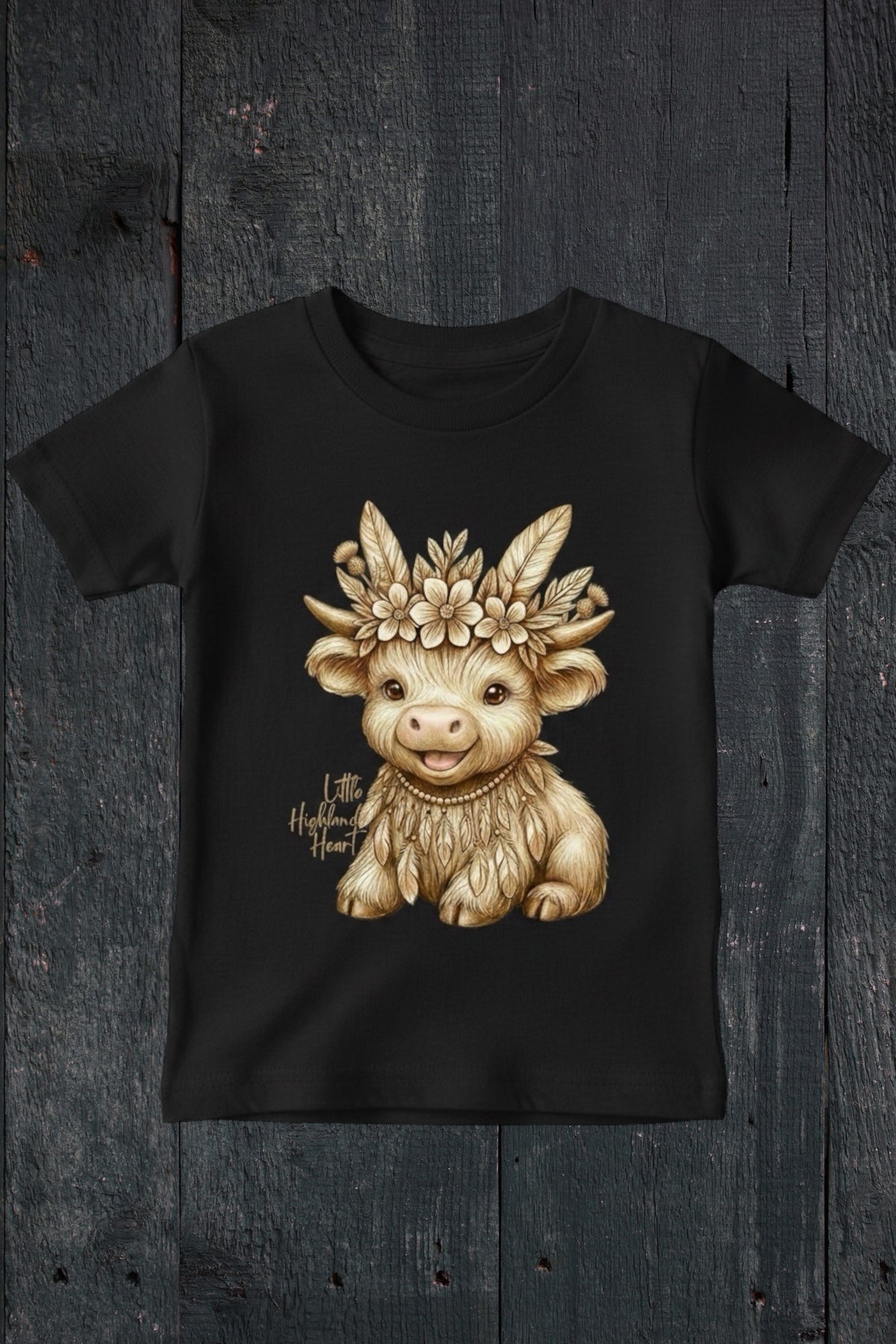 Flat lay of Fox and Form Thistle the Boho Highland Calf black classic ring spun tee with hand-illustrated boho highland calf design and Little Highland Heart script on a dark wood background