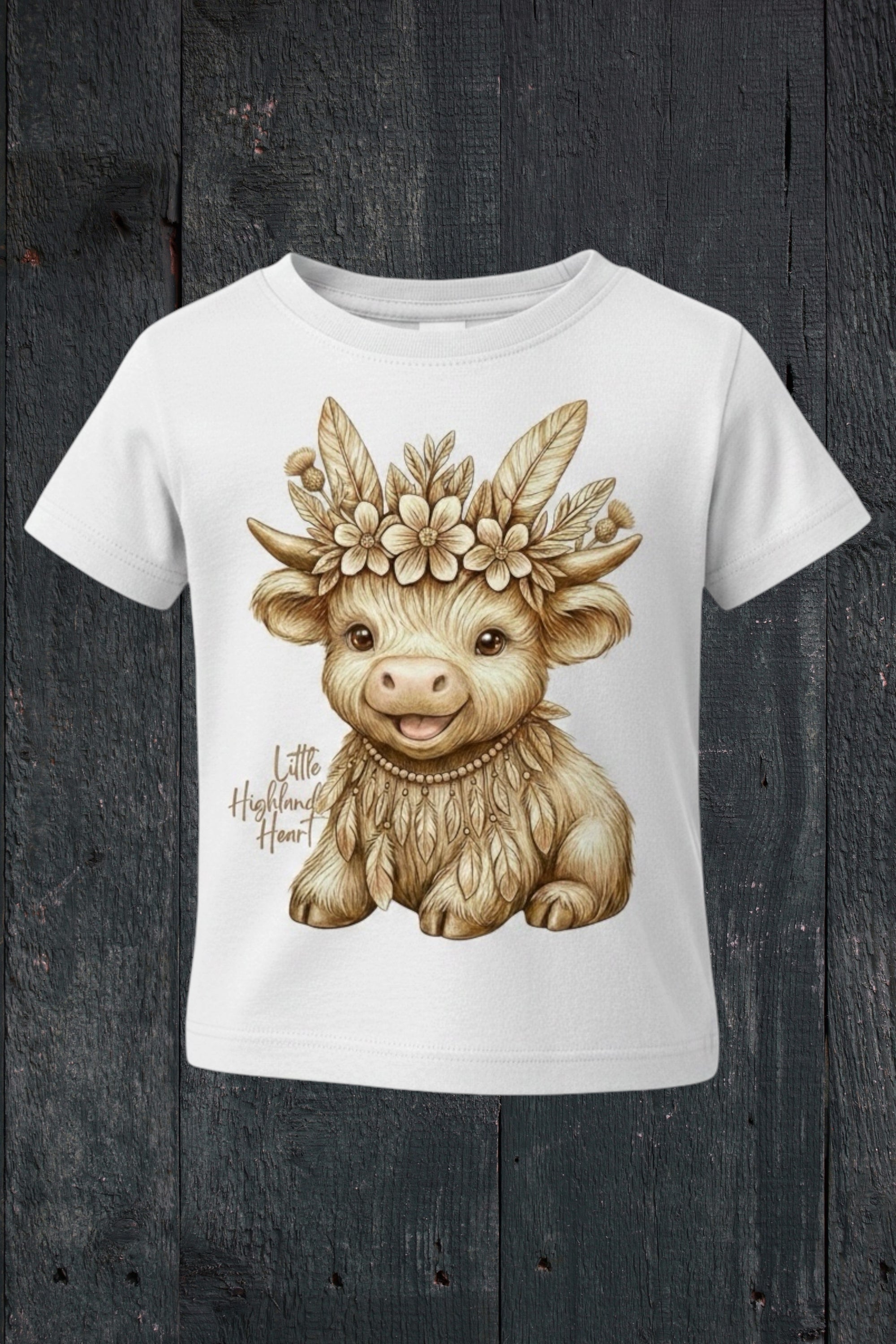 Flat lay of Fox and Form Thistle the Boho Highland Calf white classic ring spun tee with hand-illustrated boho highland calf design and Little Highland Heart script on a dark wood background