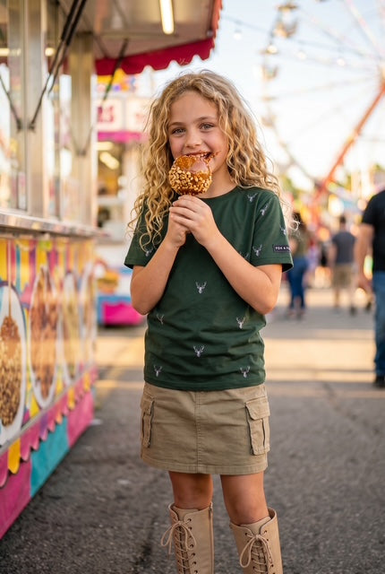 Young girl eating a caramel apple at a summer fair wearing Fox and Form The Stag forest green classic ring spun tee with hand-etched illustrated stag pattern design